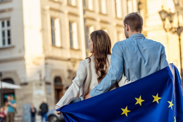 back view of young couple, wrapped in flag of european union, standing on street